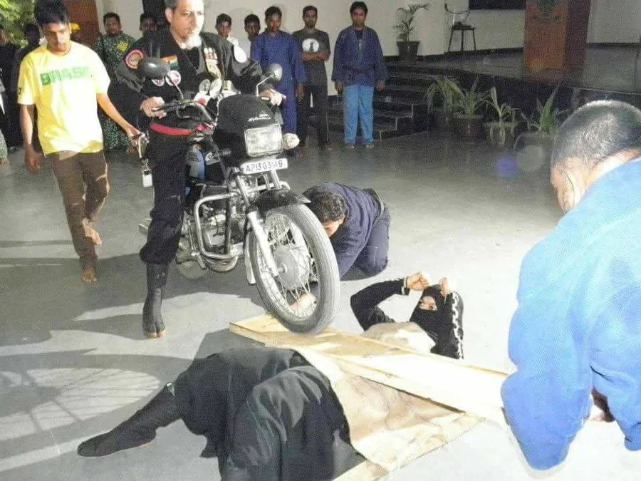 Motorcycle ridden over boards resting on two students in a hall